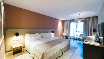 Habitación de hotel con una cama grande, mesitas de noche, un escritorio con silla, televisor y ventana con cortinas.