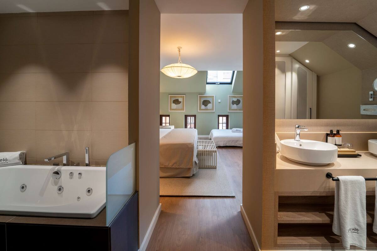 Een moderne badkamer met een groot bad, een wastafel en een spiegel. Er is een handdoekhouder met een handdoek eraan. De badkamer heeft houten vloeren en een lamp aan het plafond.