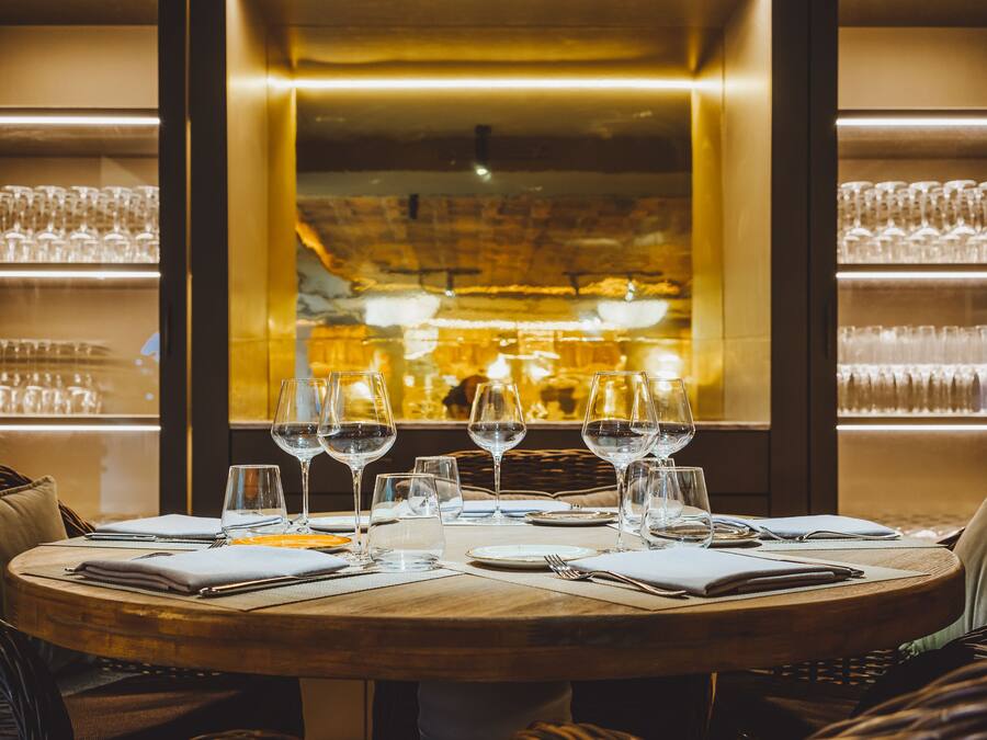 Un salón de restaurante con una mesa redonda preparada para comer, vasos y cubiertos.