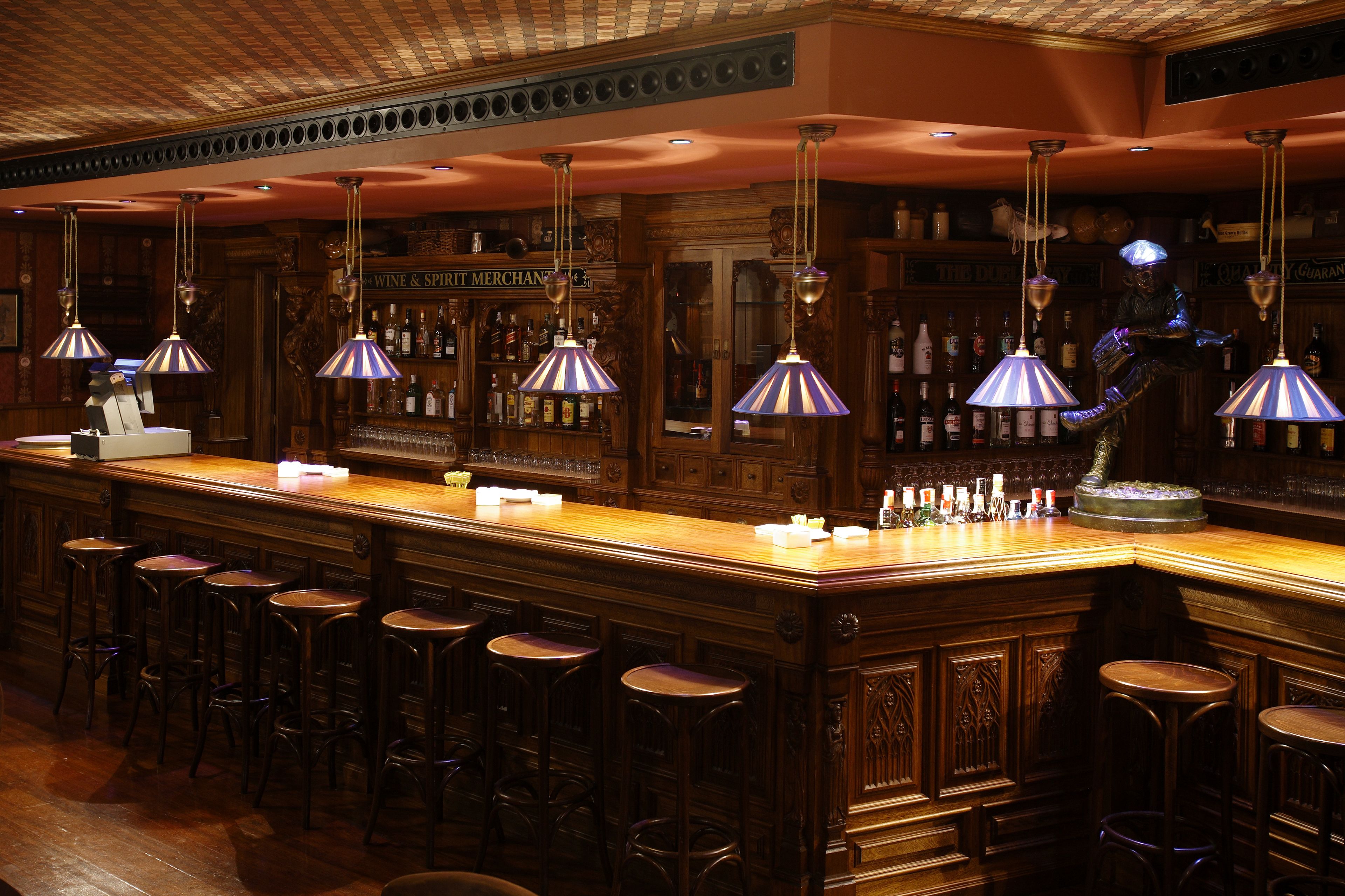 A bar area with multiple stools, hanging lamps, and a well-stocked liquor shelf.