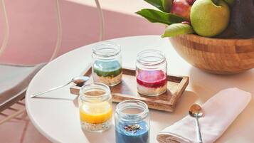 Ein Tisch mit vier Gläsern, die farbenfrohe, geschichtete Desserts enthalten, einer Holzschüssel mit Früchten und einem Löffel auf einer Serviette.