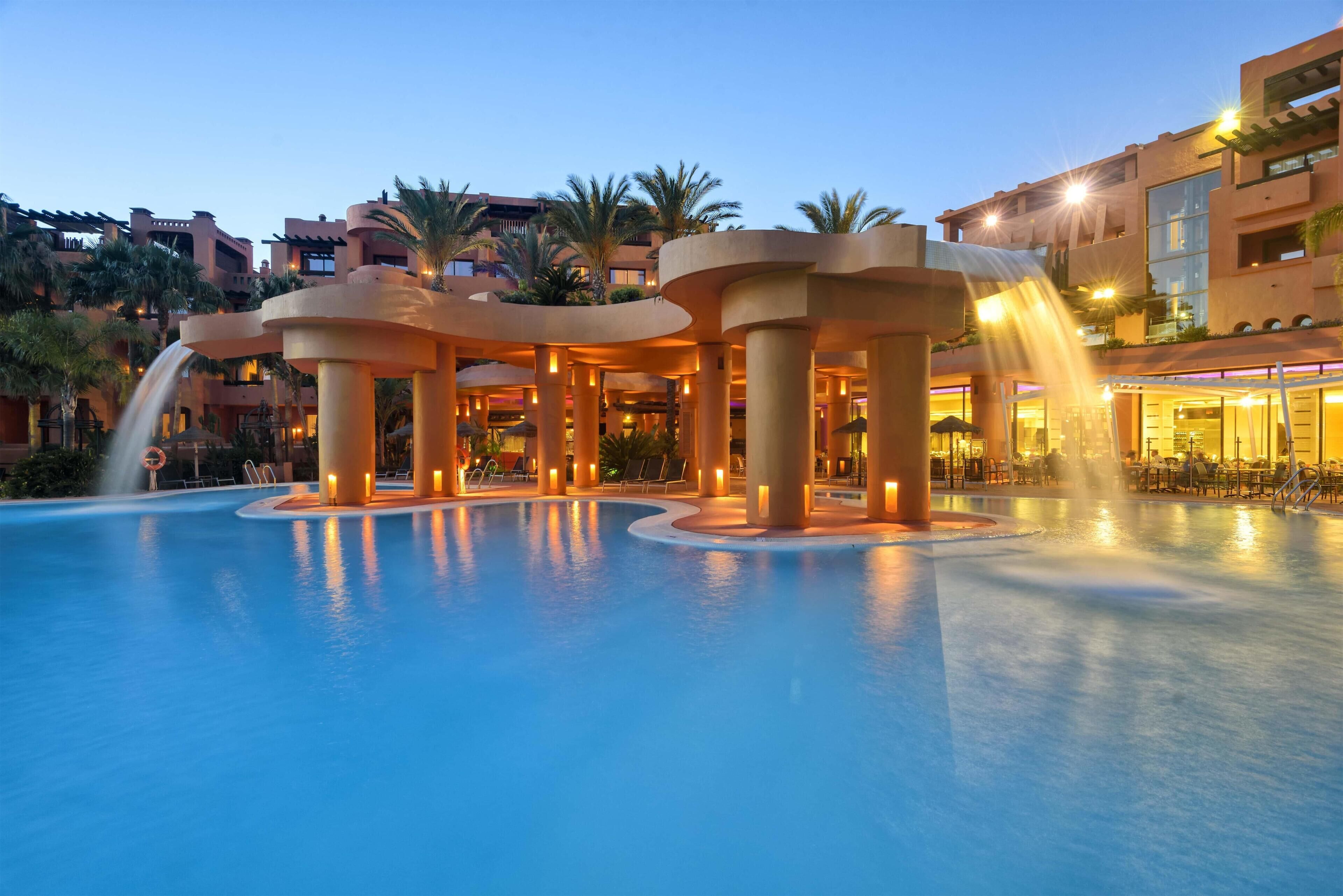 Un área de piscina con múltiples fuentes de agua y un edificio con balcones.