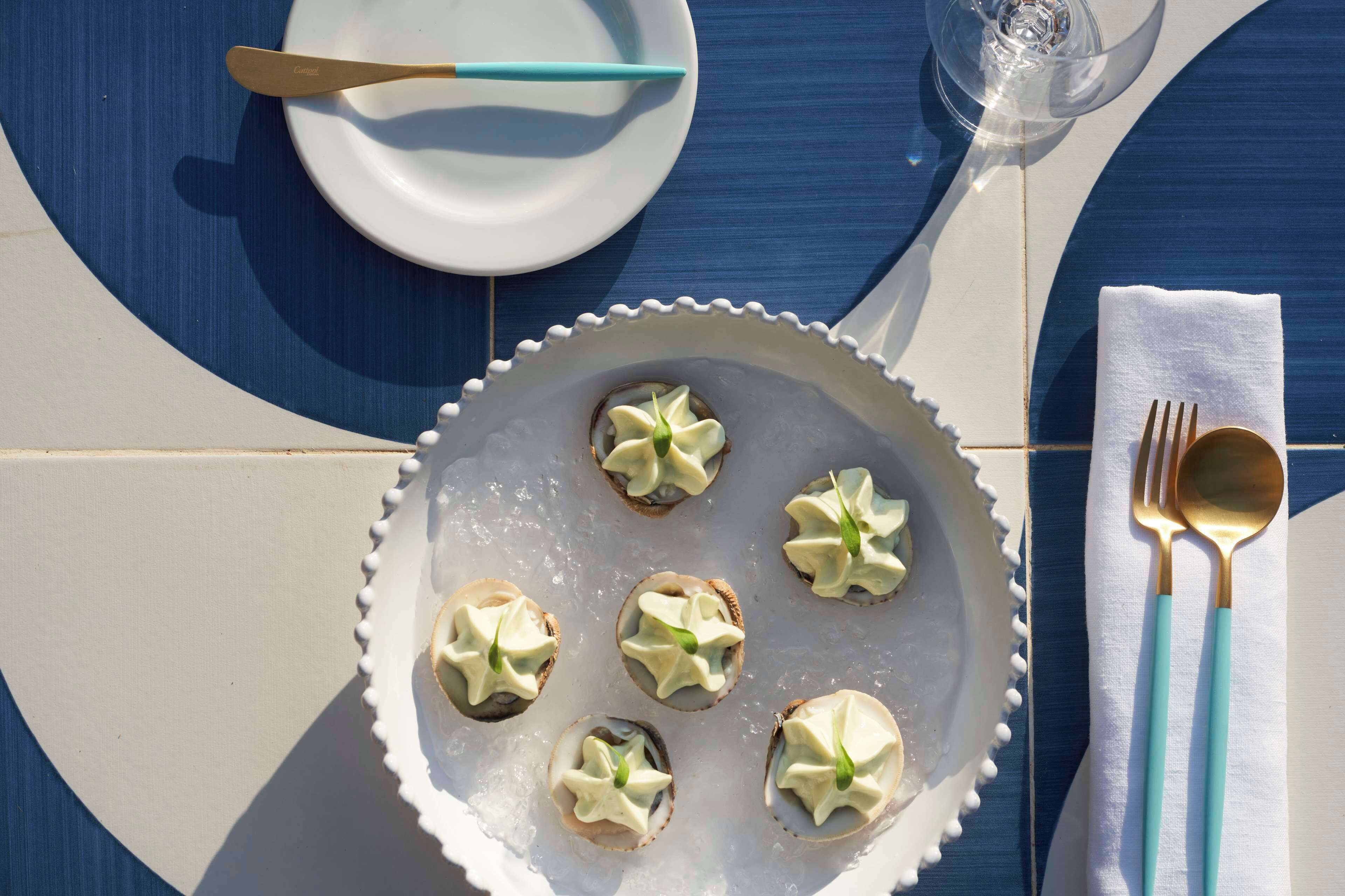 Un tavolo con un piatto bianco pieno di pasticcini a forma di stella, un bicchiere d'acqua e un tovagliolo bianco con un manico azzurro.