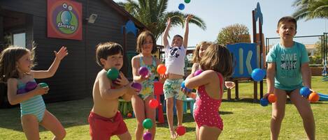 Children playing with balls in a grassy area with a building in the background.
