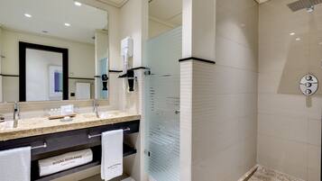 Un baño moderno con ducha revestida de baldosas color beige, puerta de vidrio y tocador con un perchero identificado como "ROYAL HIDEAWAY".