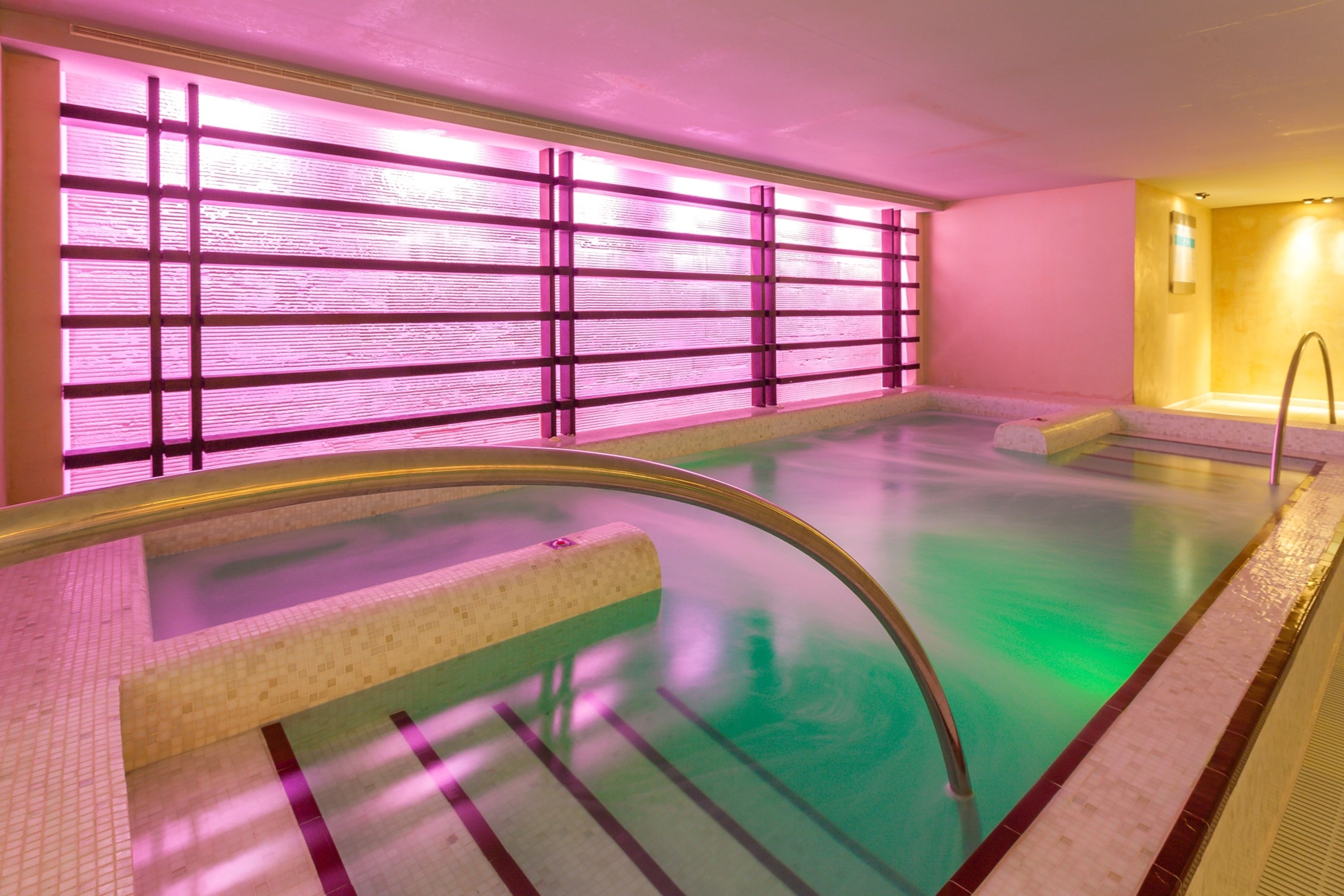 Ein Wellnessbereich mit großem Pool, Glastrennwand und Fliesenboden.