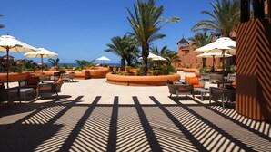 Eine Resort-Terrasse mit Sitzgelegenheiten im Freien, Palmen und Blick auf den Ozean.