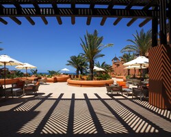 Un patio de resort con mobiliario exterior, palmeras y vista al océano.
