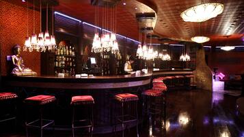 A bar area with a curved counter, multiple hanging chandeliers, and bar stools with red cushions.