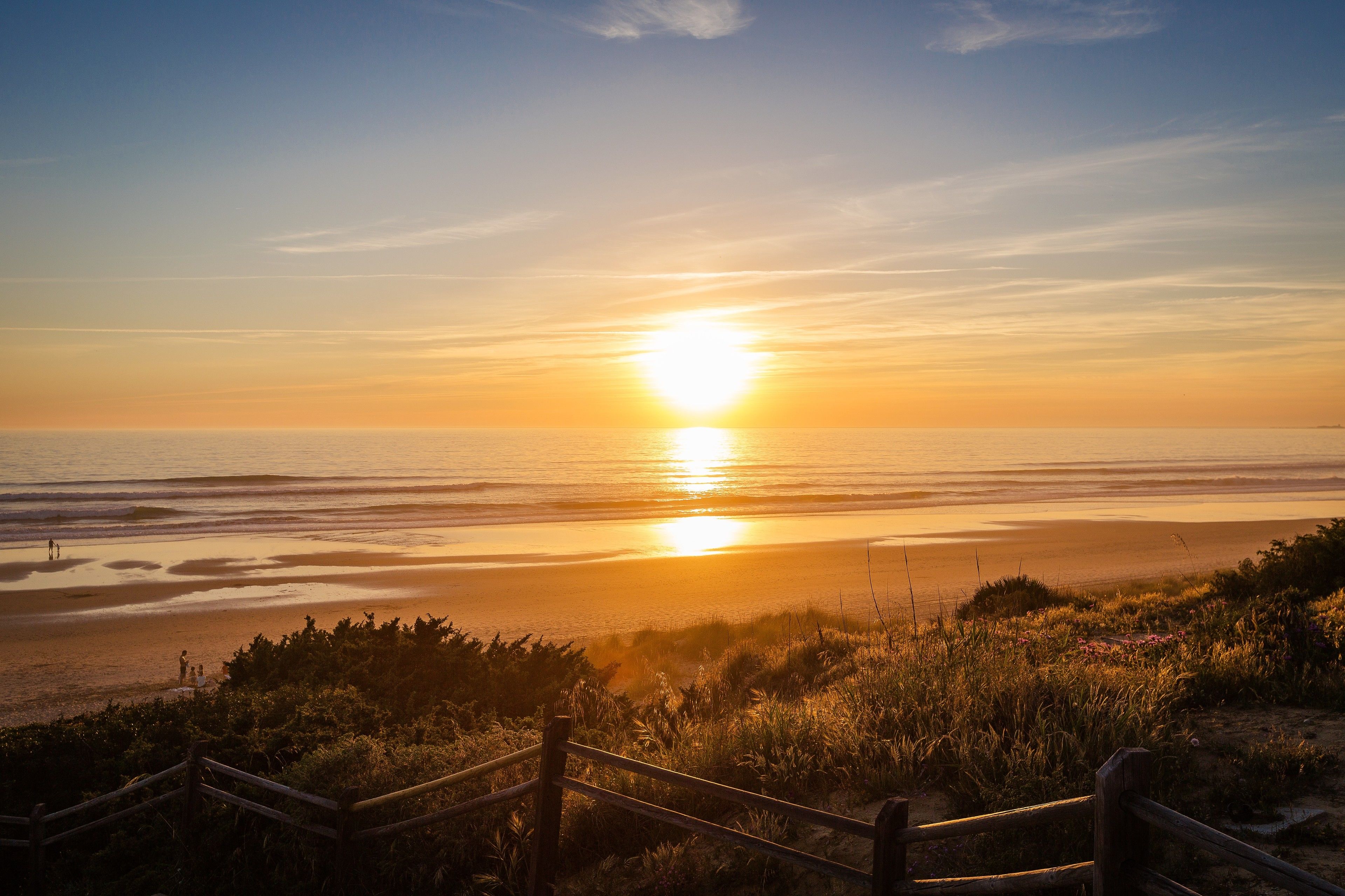 A sunset over a beach with a wooden fence in the foreground.