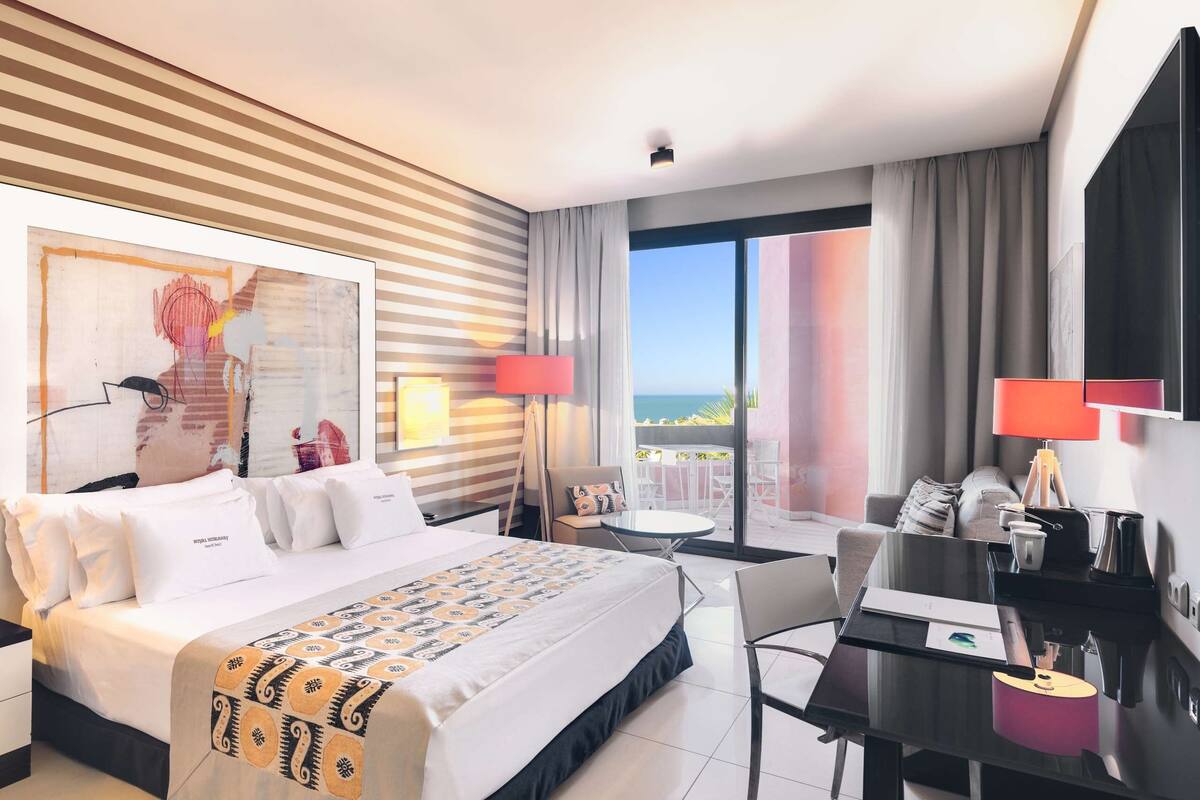 Une chambre d’hôtel moderne dotée d’un grand lit, d’un bureau et d’un balcon avec vue.
