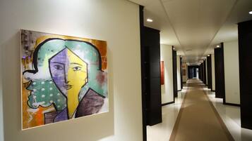 A hallway with a long corridor, a framed artwork on the wall, and a carpeted floor.