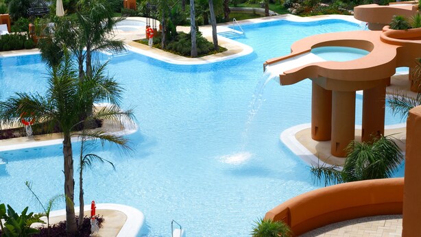 Ein Resort mit großem Pool, umgeben von Palmen und Blick auf den Ozean.