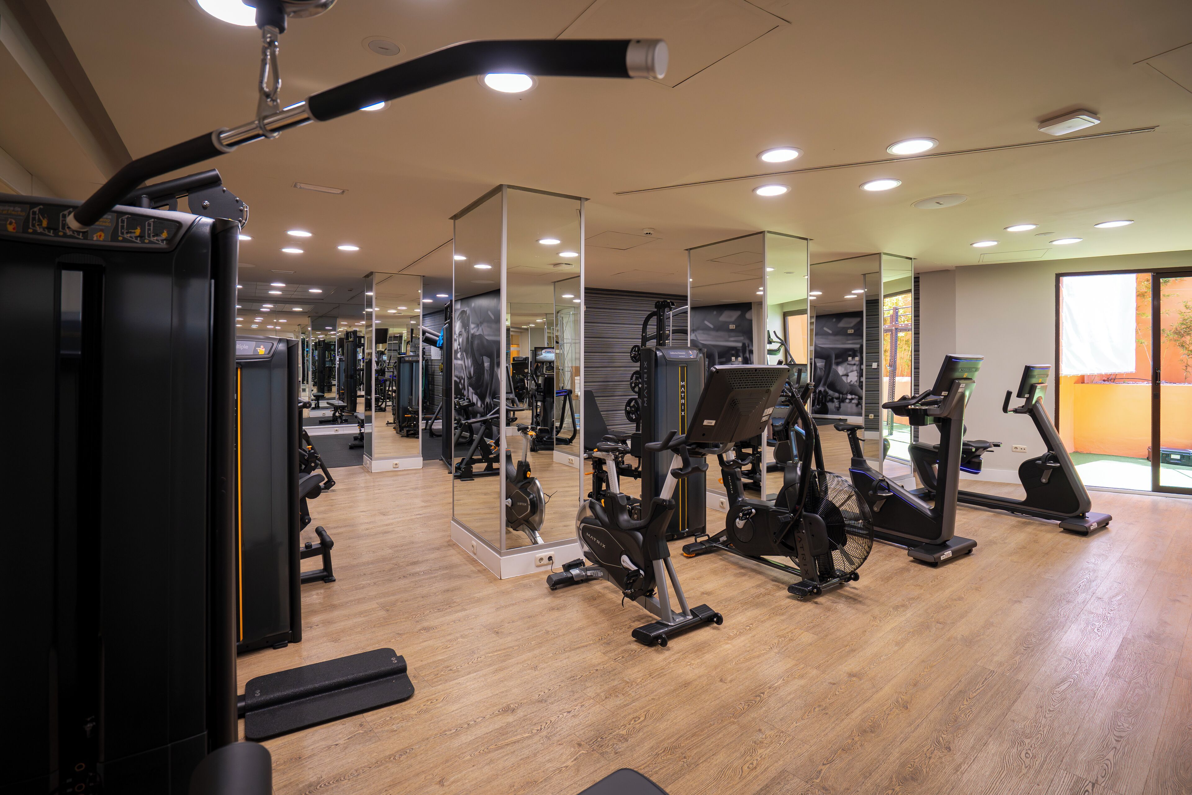 A gym with various exercise equipment, including treadmills and weight machines, and a wooden floor.