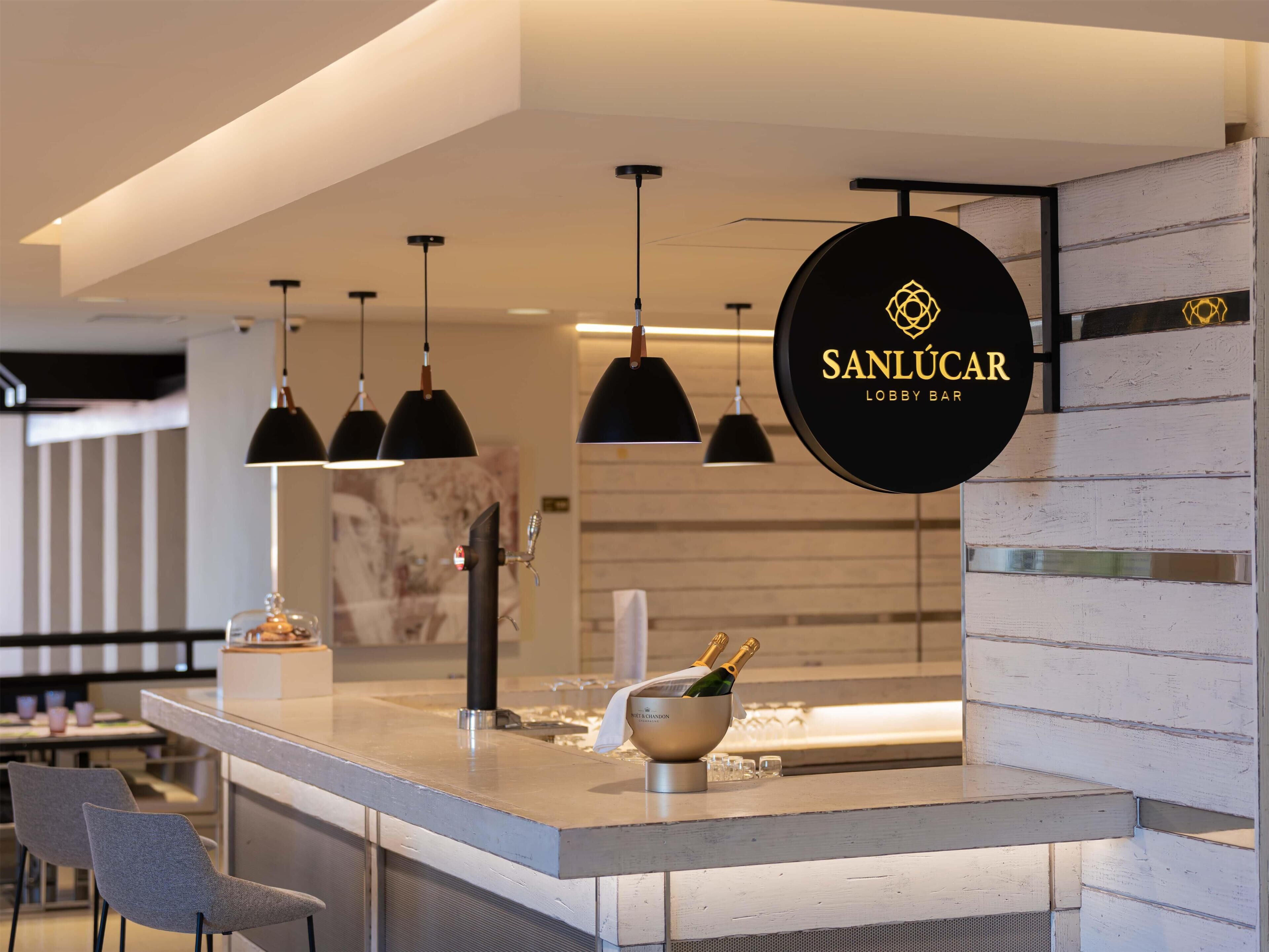 Eine moderne Bar mit Pendelleuchten, einer Bar und einem Schild mit der Aufschrift 'SANLUCAR LOBBY BAR'.