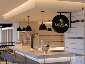 A modern bar area with pendant lighting, a bar counter, and a sign reading 'SANLUCAR LOBBY BAR'.