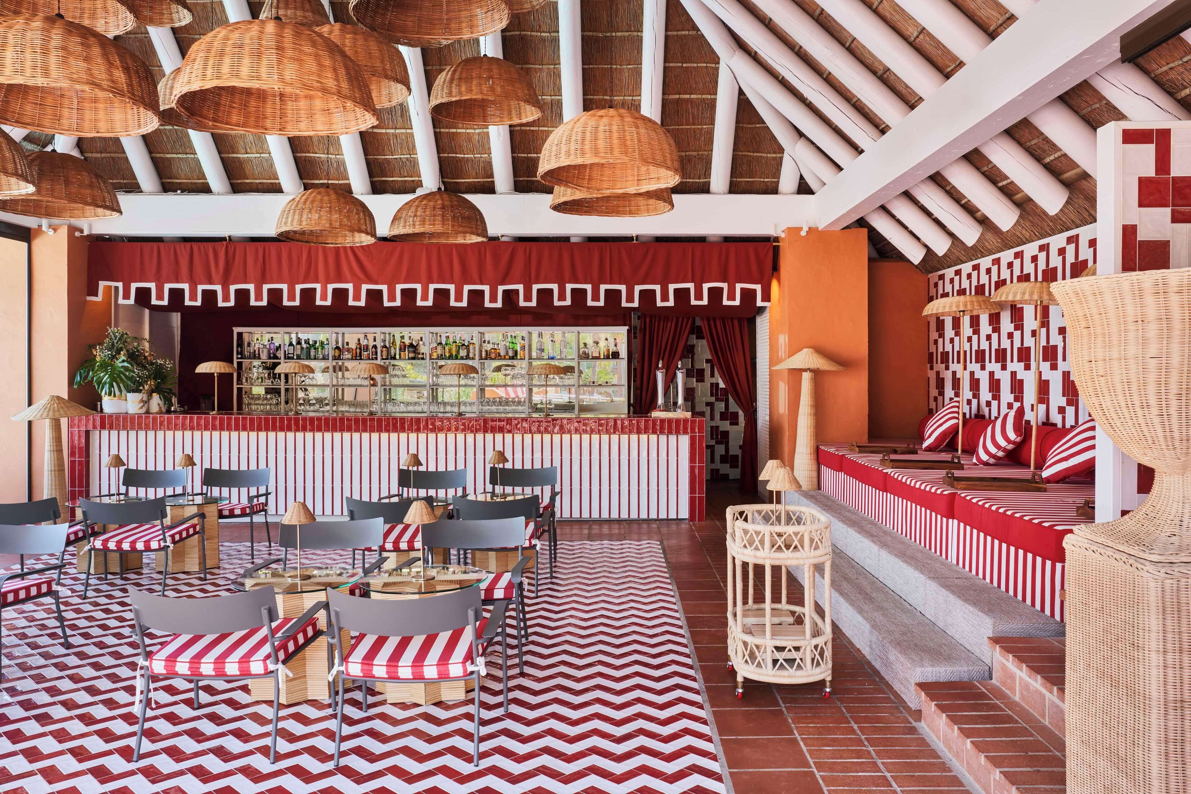 Un restaurant avec des meubles en osier, une décoration à rayures rouges et blanches, et un coin bar où sont exposées des bouteilles.