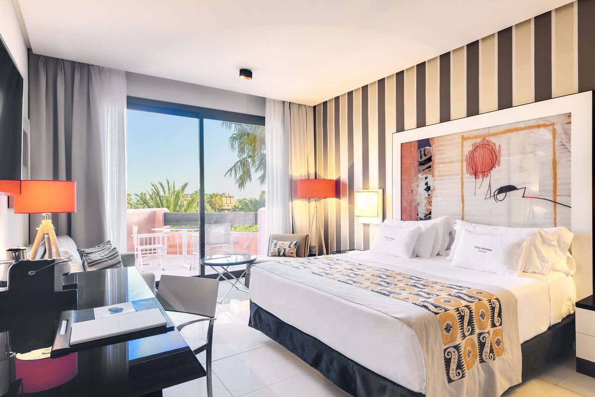 Une chambre d’hôtel moderne, dotée d’un grand lit, d’un bureau et offrant une vue sur l’extérieur.