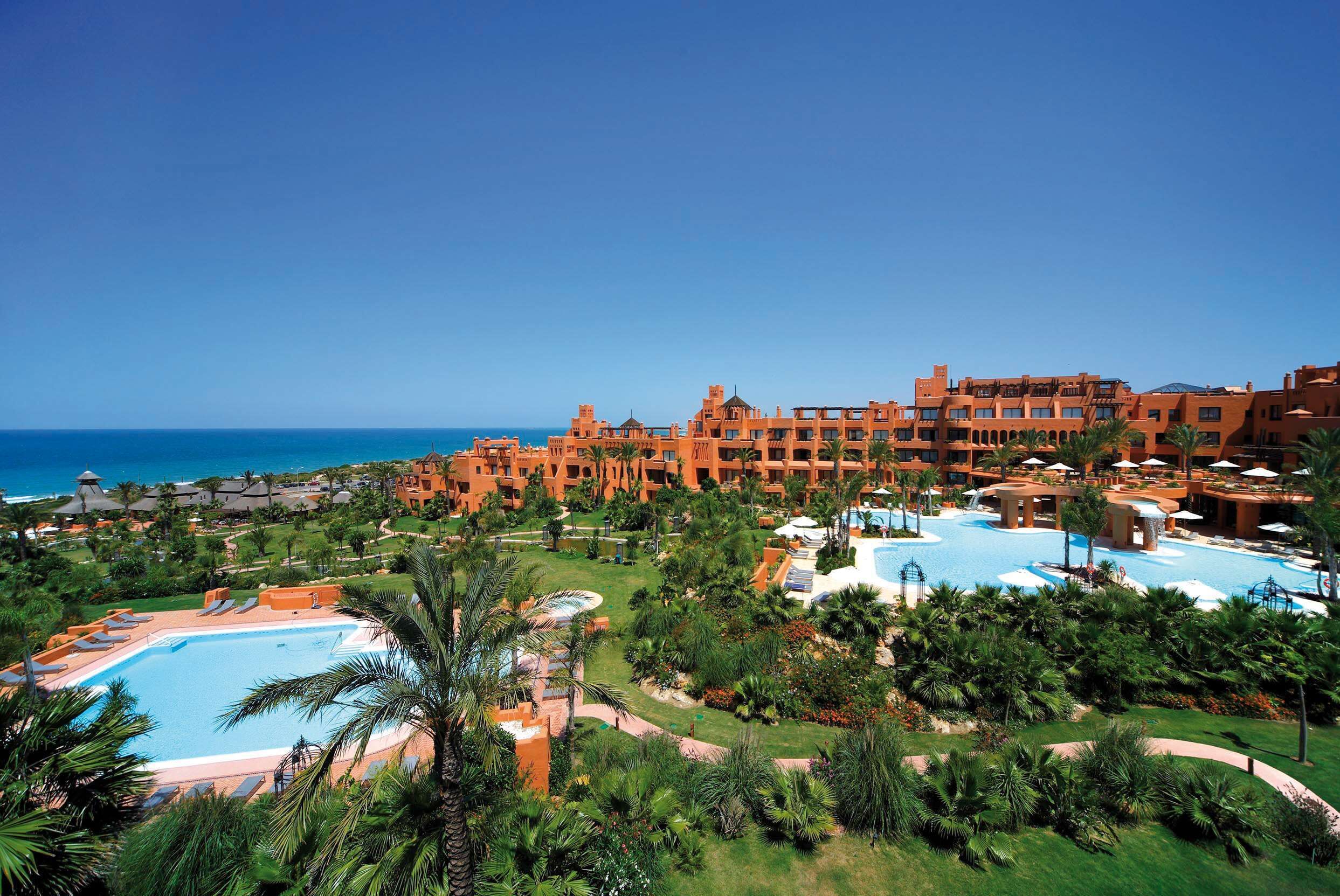 A resort with multiple swimming pools, lush greenery, and a view of the ocean.