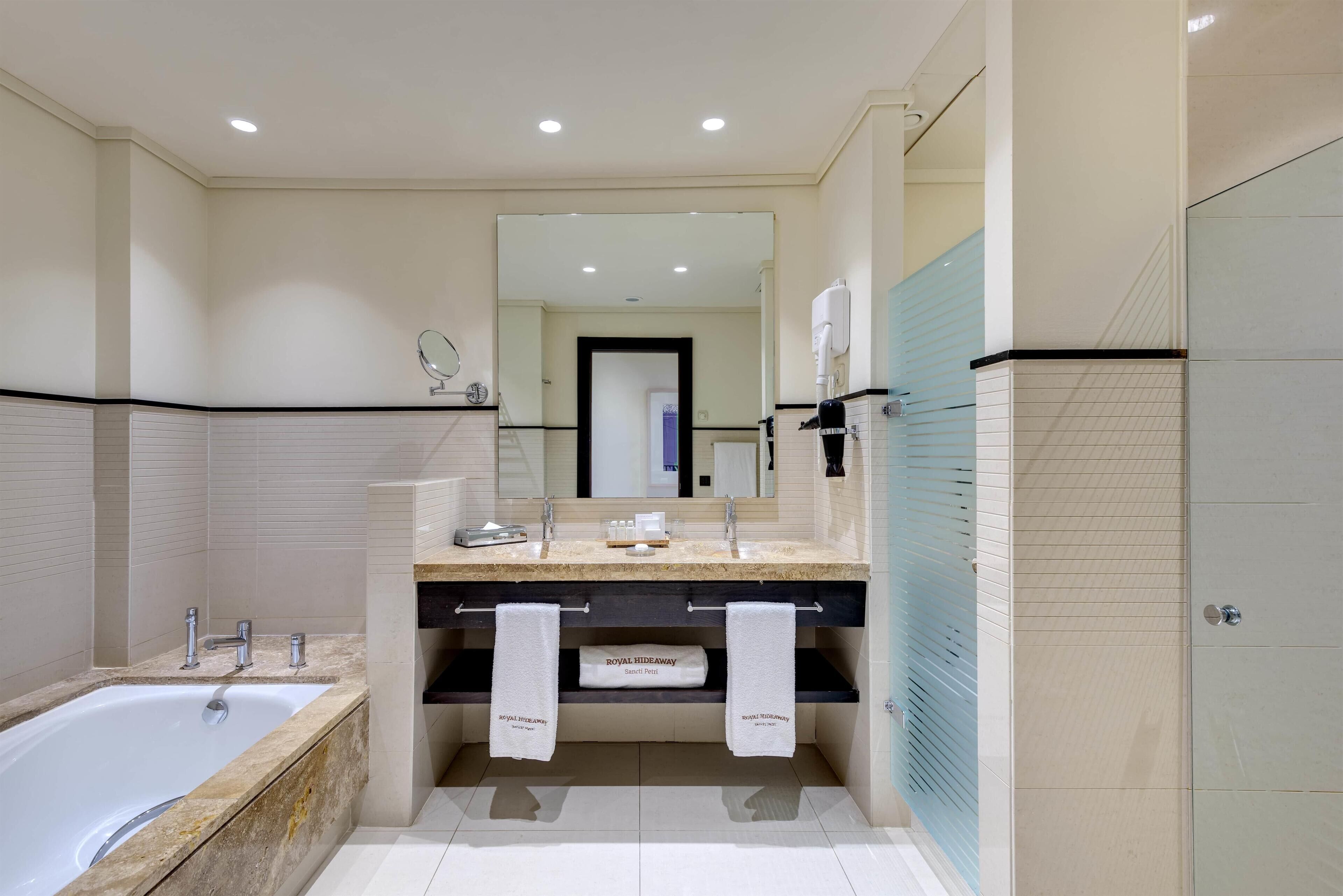 Un baño moderno con bañera, tocador doble y un espejo grande.
