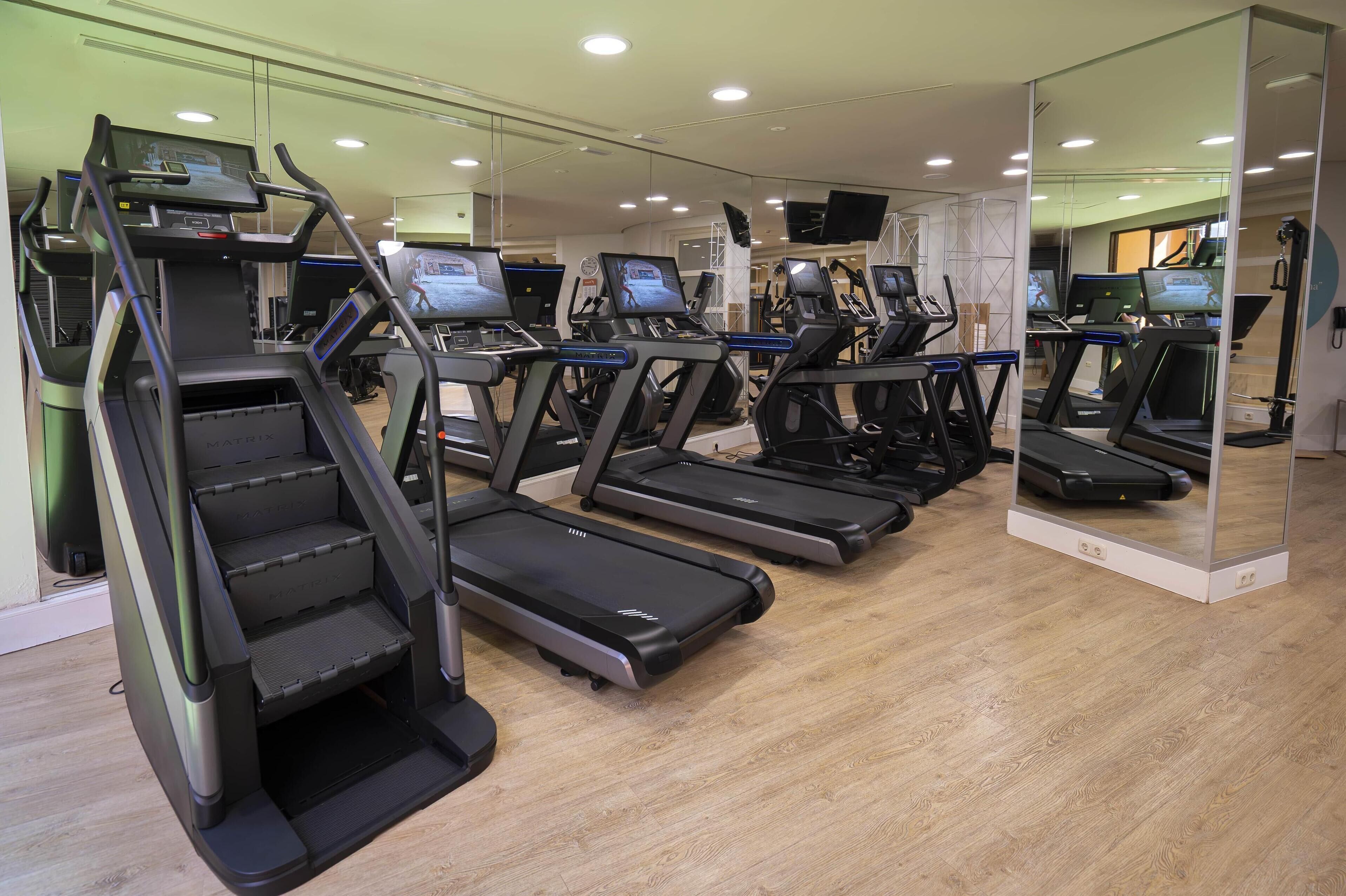 Ein Fitnessstudio mit mehreren Laufbändern, einer Spiegelwand und Holzboden.