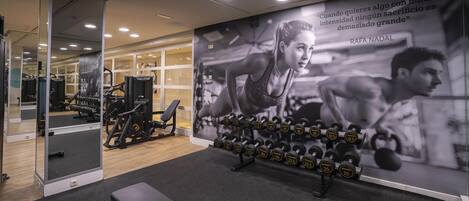 Un gimnasio con equipo de ejercicio, una banca y una frase motivadora en la pared.