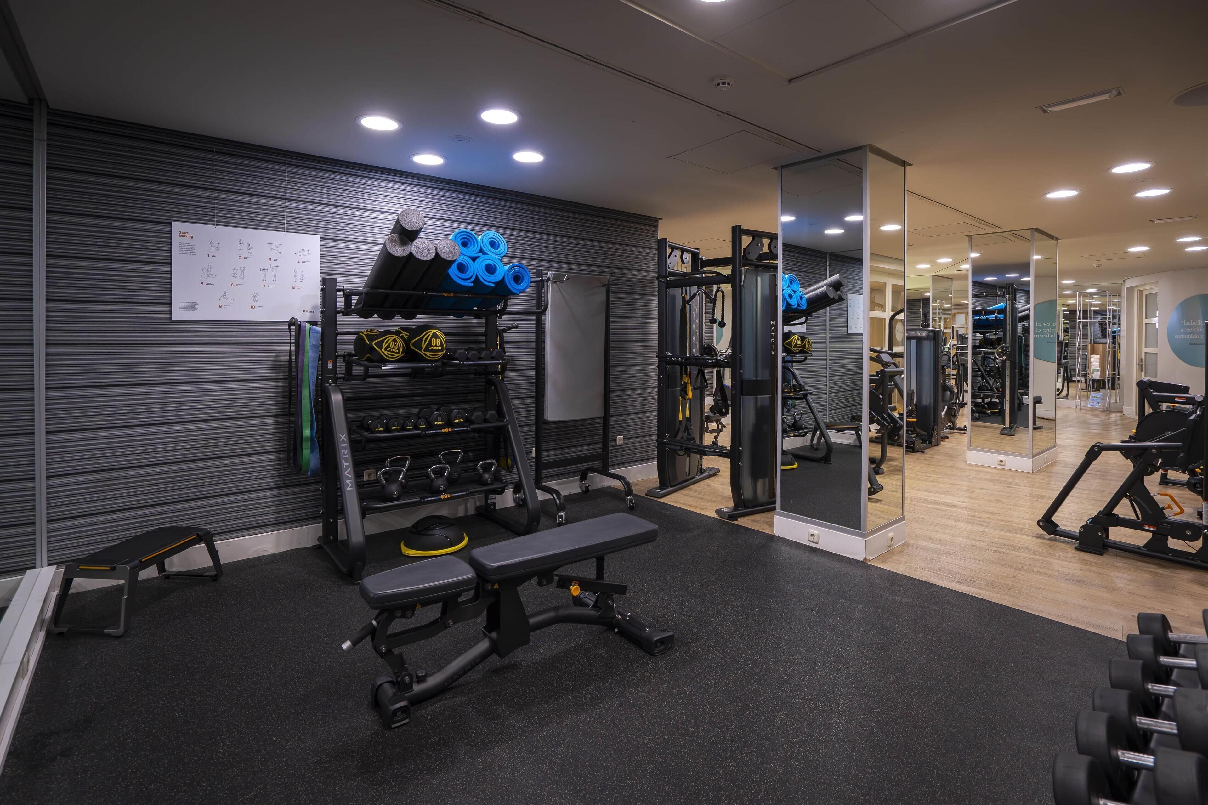 A gym with weightlifting equipment, benches, and a mirrored wall.