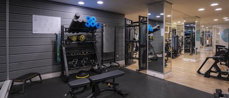 A gym with weightlifting equipment, benches, and a mirrored wall.
