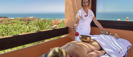 A massage therapy session on a balcony overlooking a coastal view.