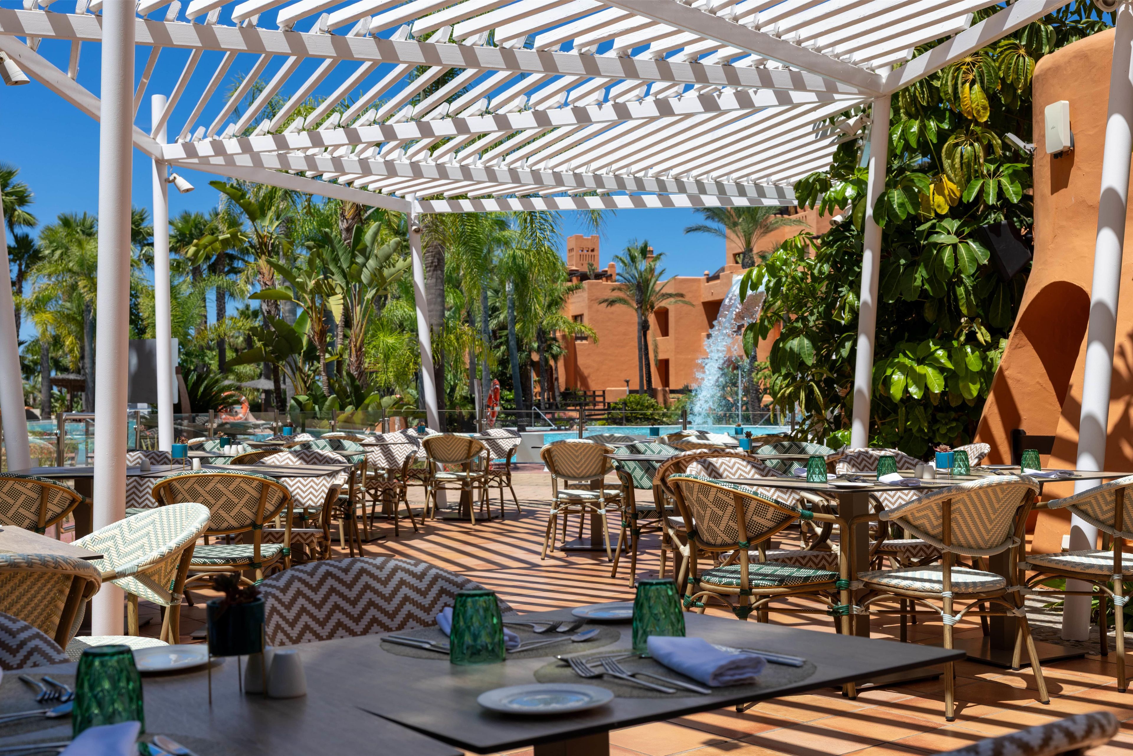 An outdoor dining area with tables and chairs, a pool, and palm trees.