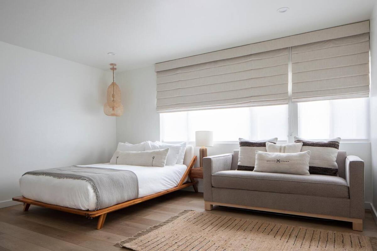 A bedroom with a bed, a sofa, a hanging light, and large windows.