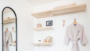 Un baño con un banco de madera, un espejo, estantes con artículos de aseo y una bata colgada en la pared.