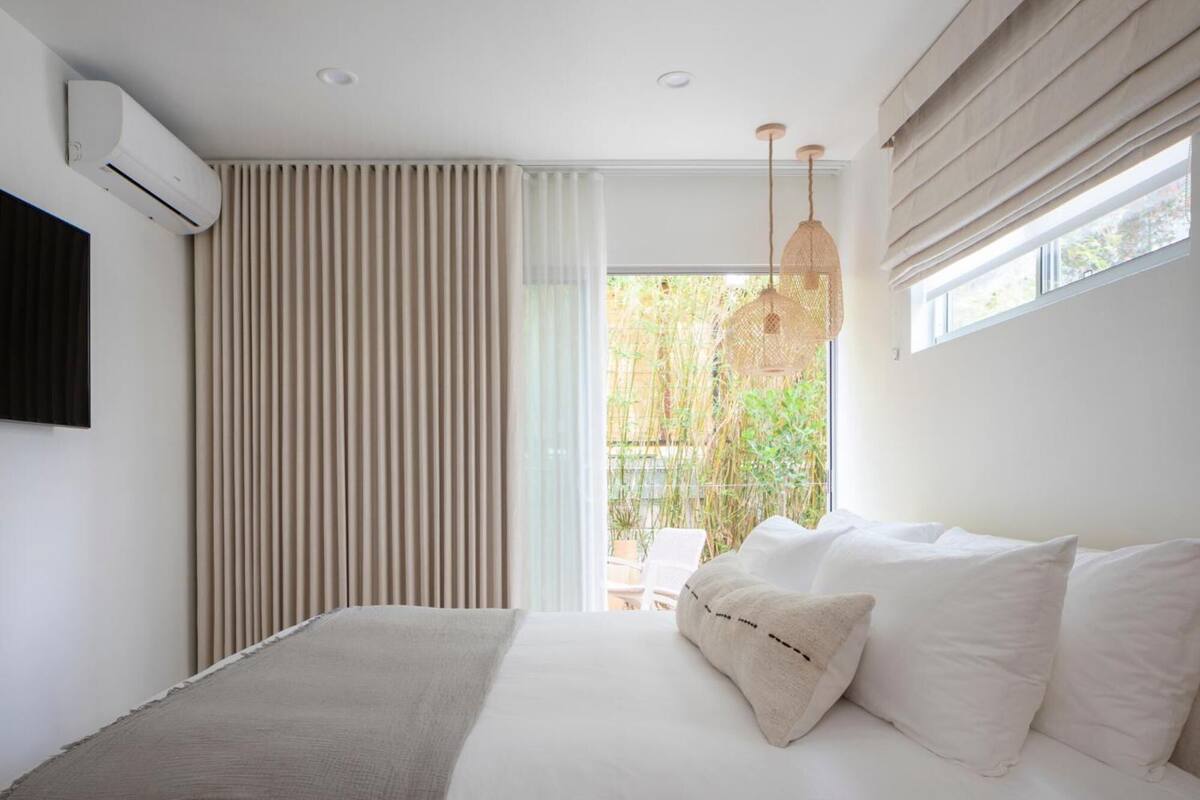 A modern bedroom with a bed, a TV mounted on the wall, and a window with curtains.