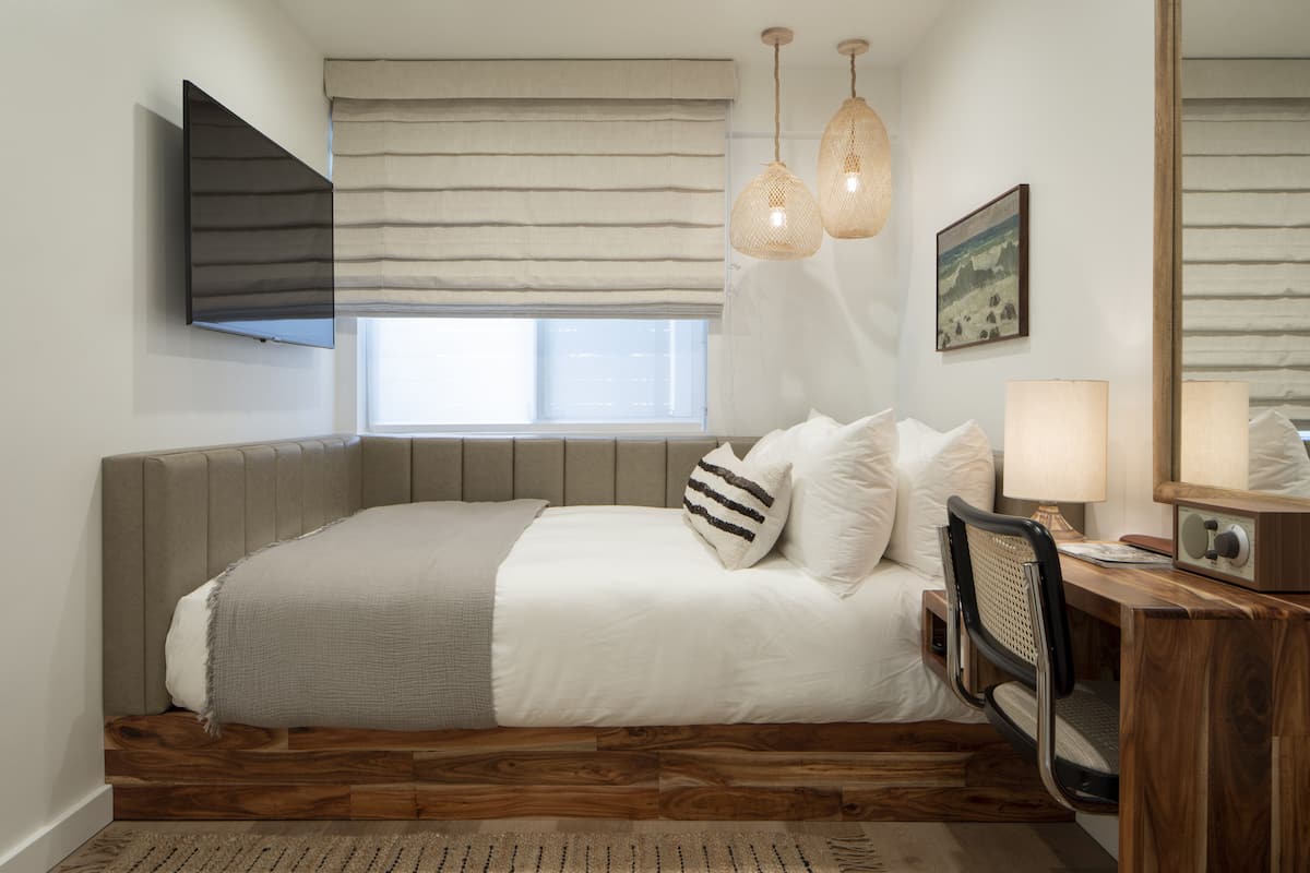 A bedroom with a bed, bedside table, lamp, and a window with curtains.
