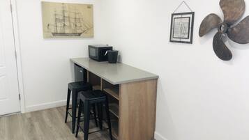 A small room with a kitchenette, two stools, a microwave, and a ship painting on the wall.