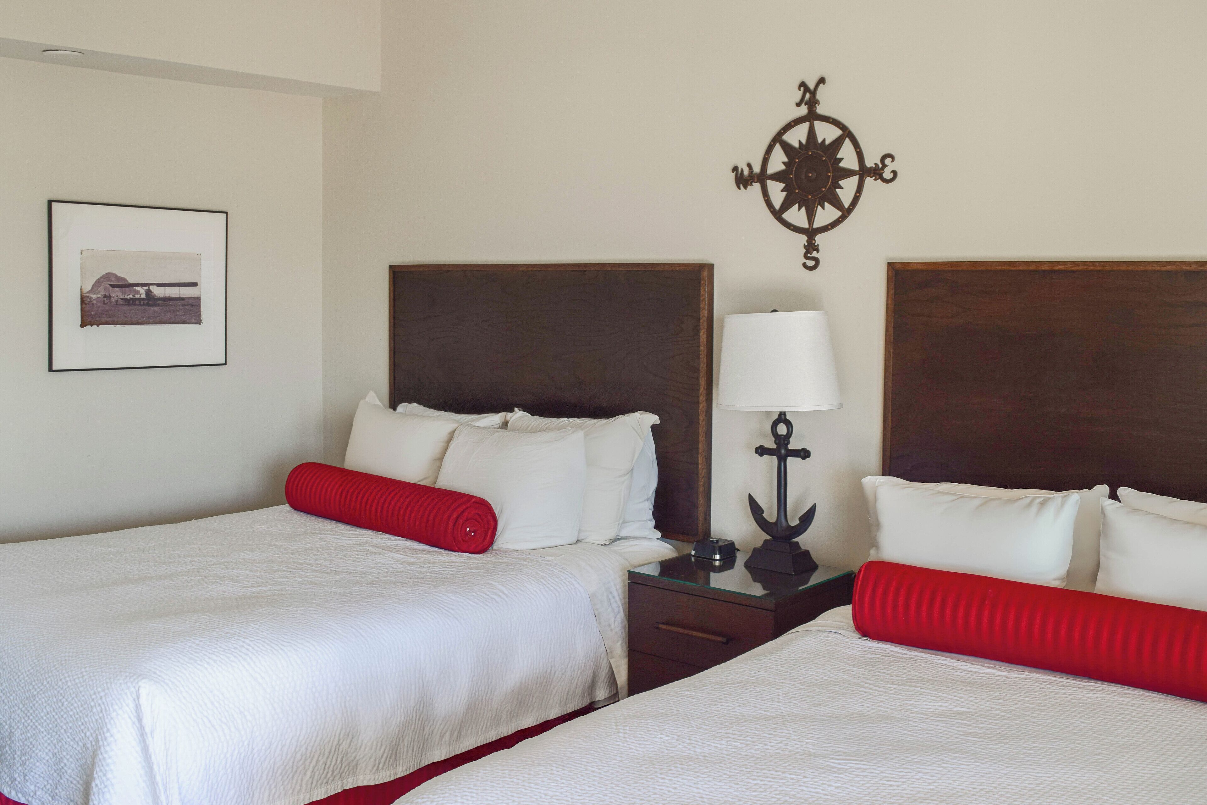 A hotel room with two beds, a nightstand with a lamp, a framed picture on the wall, and a compass decoration.