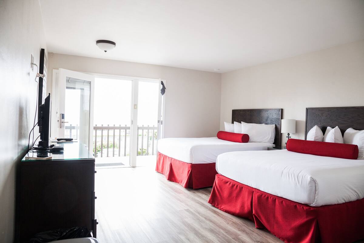 A hotel room with two beds, a desk, and a sliding door to a balcony.