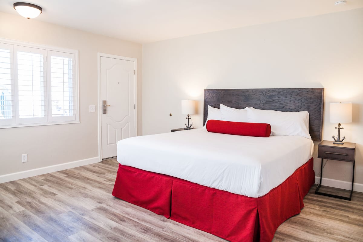 A hotel room with a large bed, a nightstand, a lamp, a door, and a window with blinds.