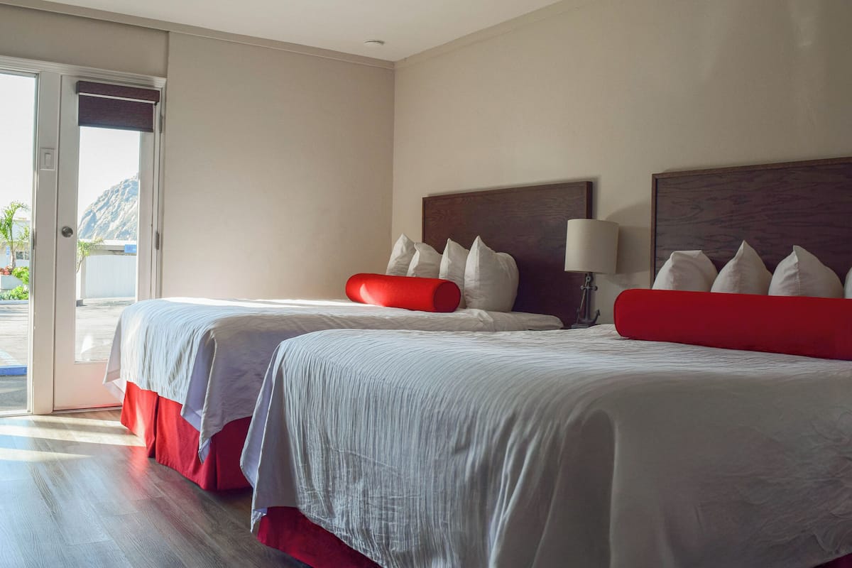 A hotel room with two beds, a large window, and a view of the outdoors.