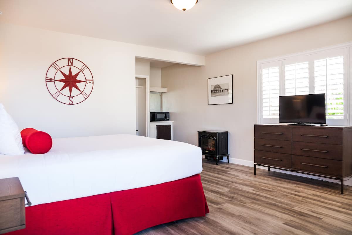 A bedroom with a large bed, a red accent pillow, a wall-mounted compass decoration, a television on a dresser, and a fireplace.