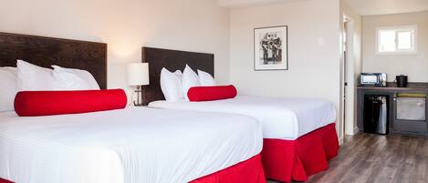 A hotel room with two beds, each with red and white bedding, a small kitchenette, and a framed picture on the wall.