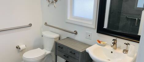 A bathroom with a toilet, a sink, a vanity, a window, and a ship's wheel decoration.