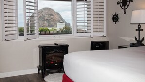 A bedroom with a bed, a window with open shutters, a wall-mounted compass, a lamp, and a small heater. - The Landing at Morro Bay (Morro Bay)