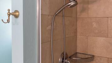Une douche équipée d’un pommeau de douche et d’un flexible à main, d’un receveur de douche en métal et d’une porte dotée d’une poignée en laiton.
