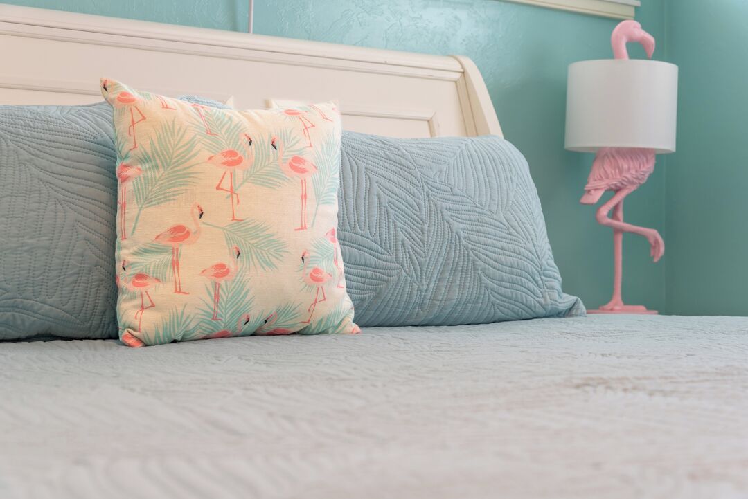 A bed with a patterned pillow and a lamp with a flamingo design.