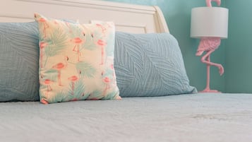 A bed with a patterned pillow and a lamp with a flamingo design.