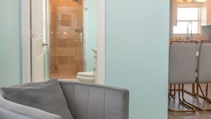Un salon moderne avec un fauteuil gris, une table basse en verre et un coin repas agrémenté d’un lustre.