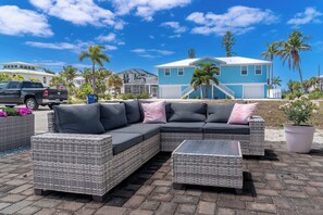 A sectional sofa with a chaise, a small table, and a wicker ottoman in an outdoor setting with a clear sky and palm trees. - Flamingo Inn (Fort Myers Beach)