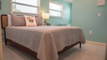 Une chambre à coucher avec un lit, deux fenêtres, une table de chevet et une lampe.