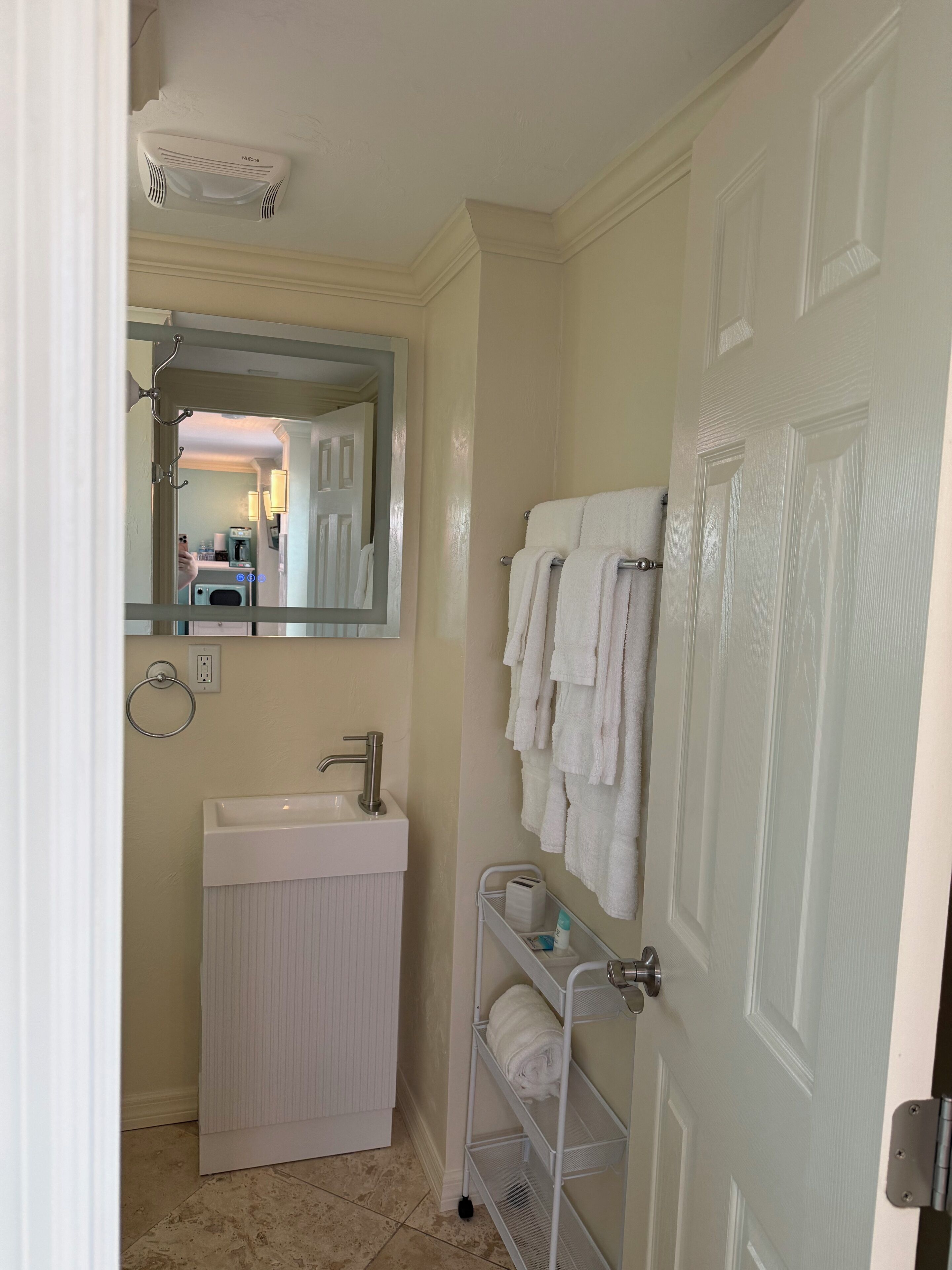 A bathroom with a white sink, a mirror, a towel rack, and a door.
